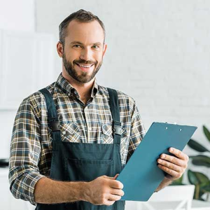 Smiling handyman in apron holding a blue clipboard in a bright workshop