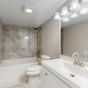 Modern bathroom with white vanity, tub, gray tile shower, and large mirror lights