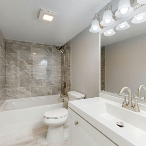 Modern bathroom with white vanity, tub, gray tile shower, and large mirror lights
