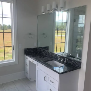 Bright bathroom vanity with black countertop, large mirror, and window view of open fields