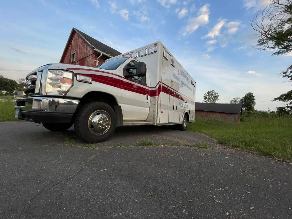 A Simsbury ambulance is parked on the side of the road in front of a barn.