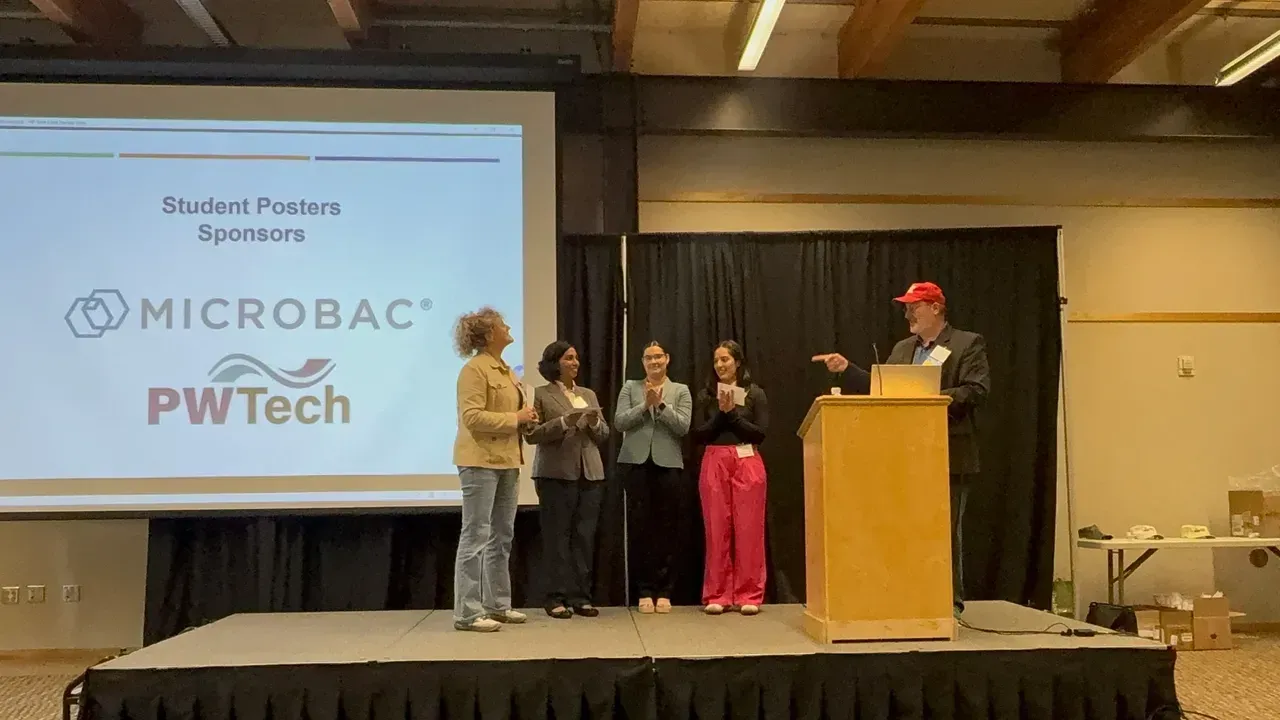 Award ceremony on stage with five speakers beside a podium and a screen showing “MICROBac PW Tech”