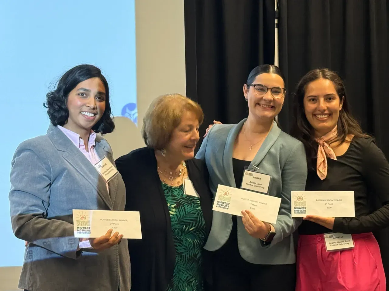 Four people smiling and holding certificates at an awards ceremony.