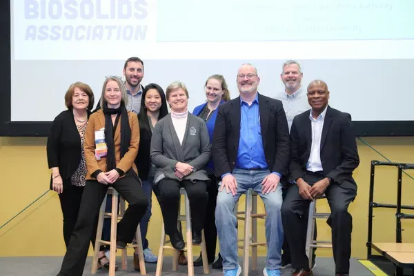 Six people seated on stools on a stage at a biosolids association event
