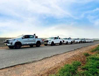 Una fila de camionetas blancas aparcadas junto a una carretera rural bajo un cielo azul