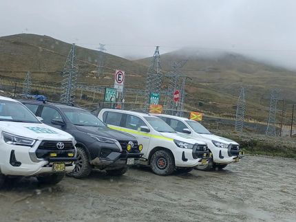 SUV blancos y oscuros aparcados en un estacionamiento de grava junto a colinas brumosas y señales de tráfico