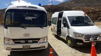 Dos furgonetas blancas estacionadas en un camino de tierra con conos naranjas, frente a una ladera rocosa y unas montañas.