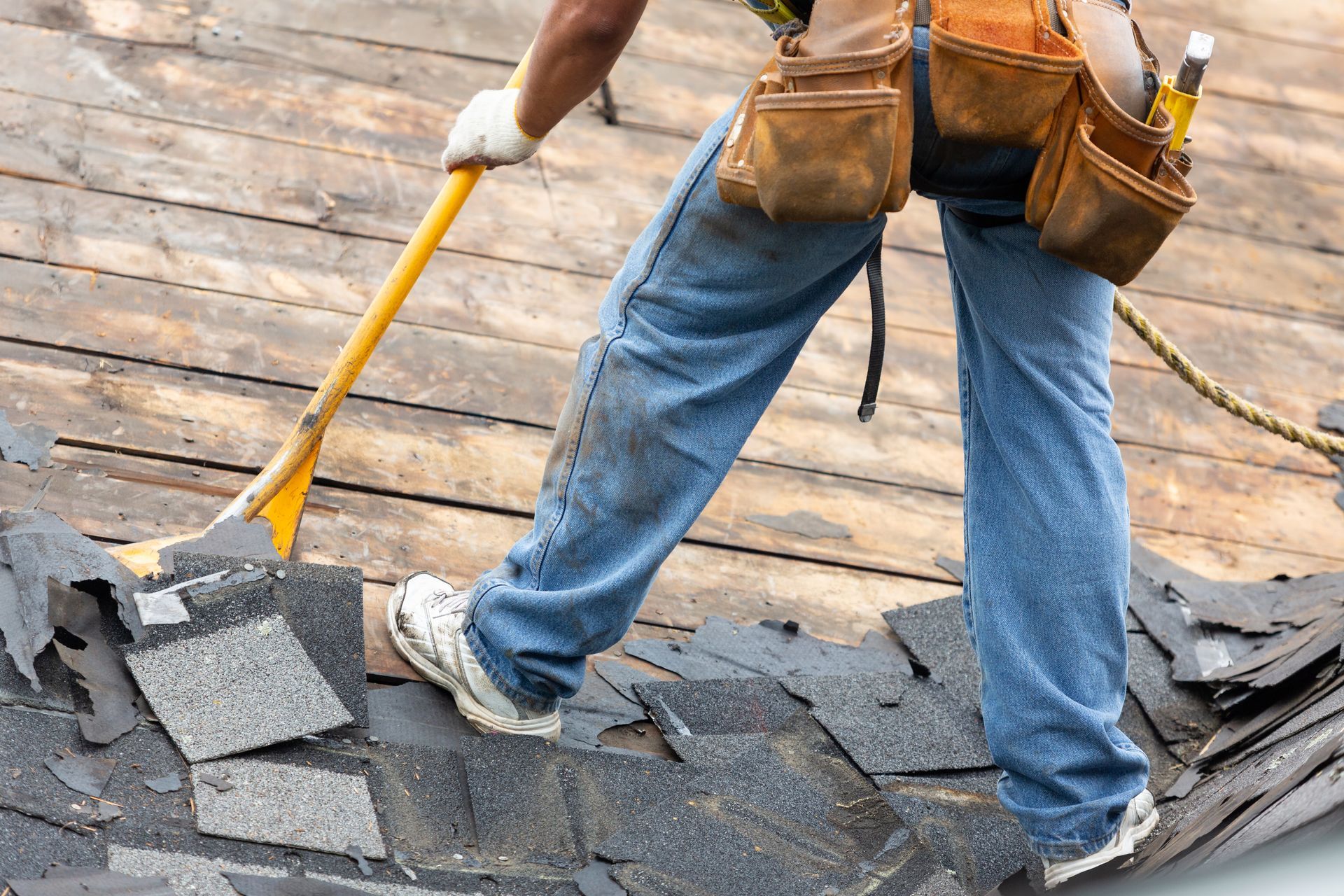 Worker removing old roof shingles with a pry bar during roof repair.