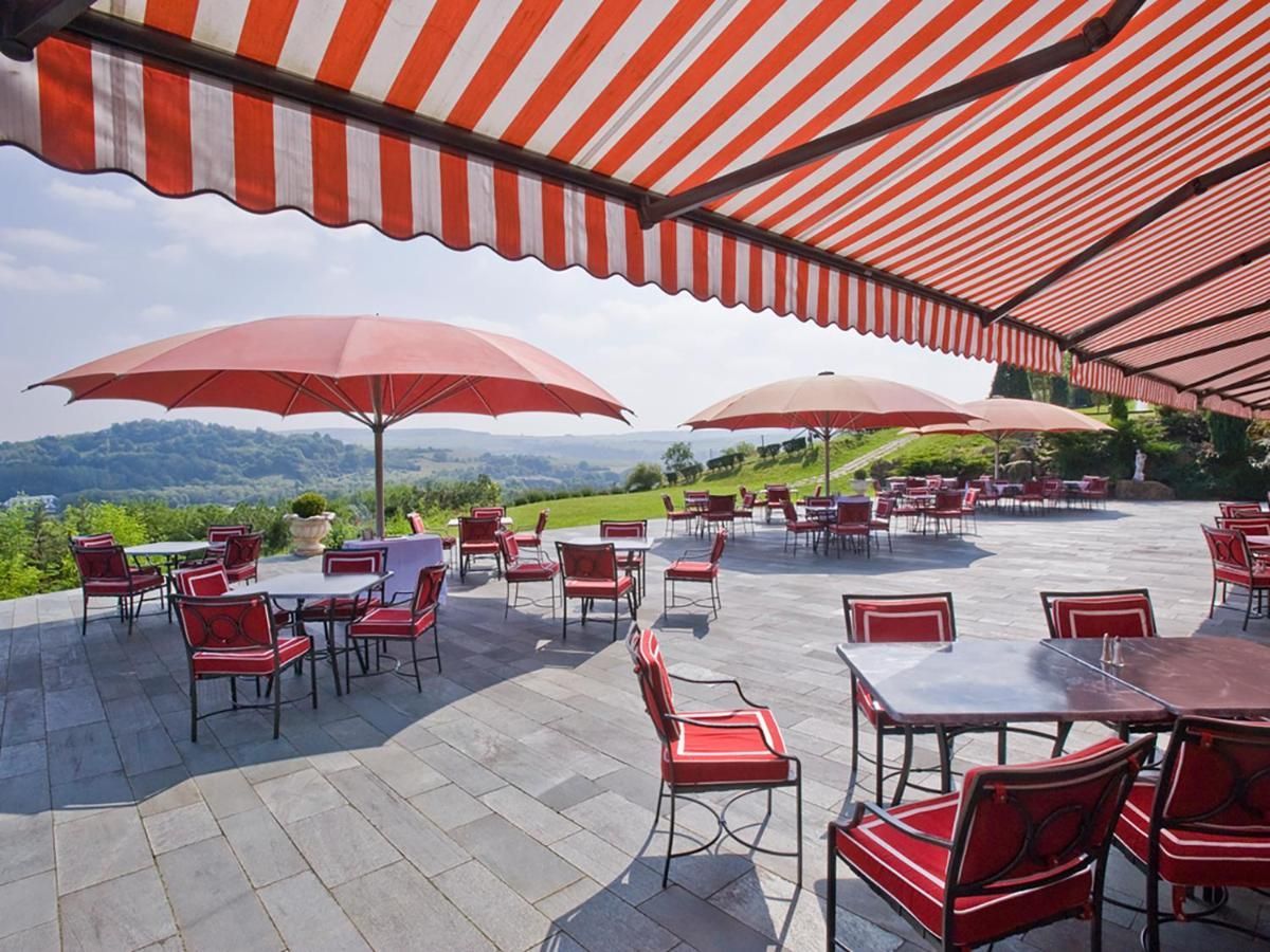 Terrasse de restaurant extérieure, tables, chaises et parasols donnant sur un paysage verdoyant.
