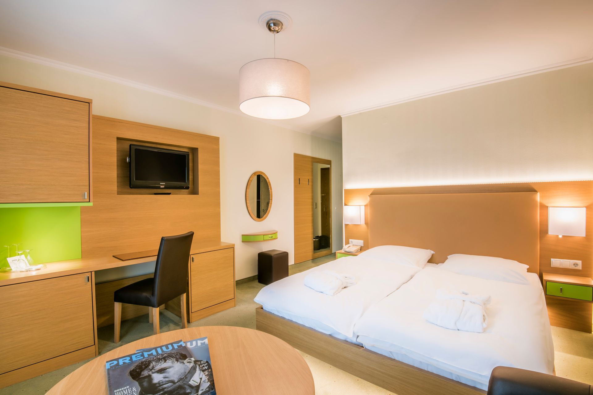 Chambre d'hôtel avec un lit, un bureau, une télévision et une table ronde avec un magazine.