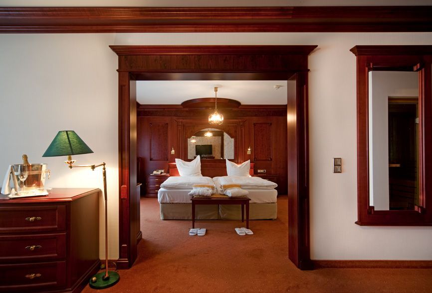Suite d'hôtel avec un lit visible à travers une porte en bois ornée.