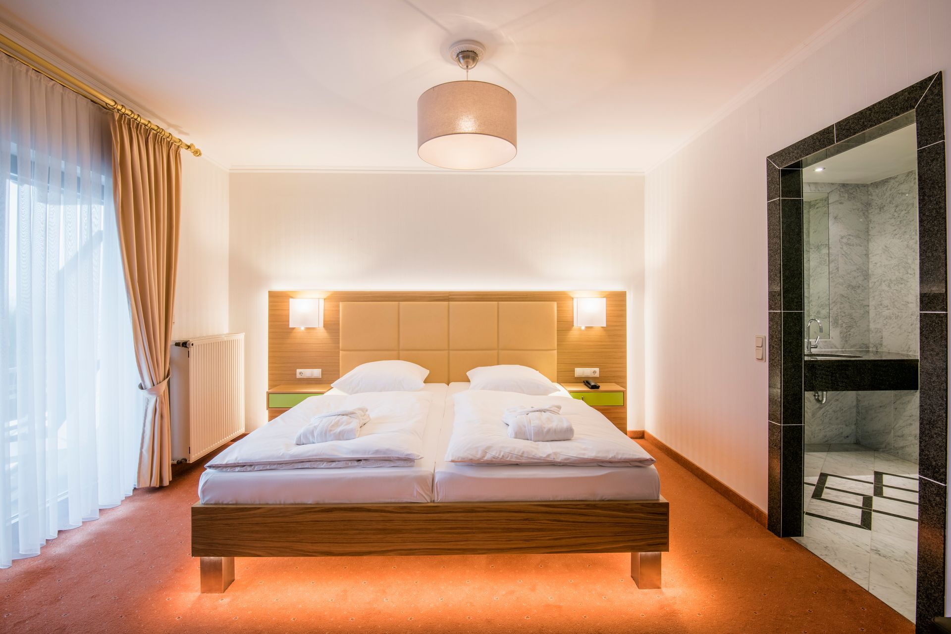 Chambre d'hôtel avec un lit double, une salle de bain et une fenêtre. La pièce bénéficie d'un éclairage chaleureux.