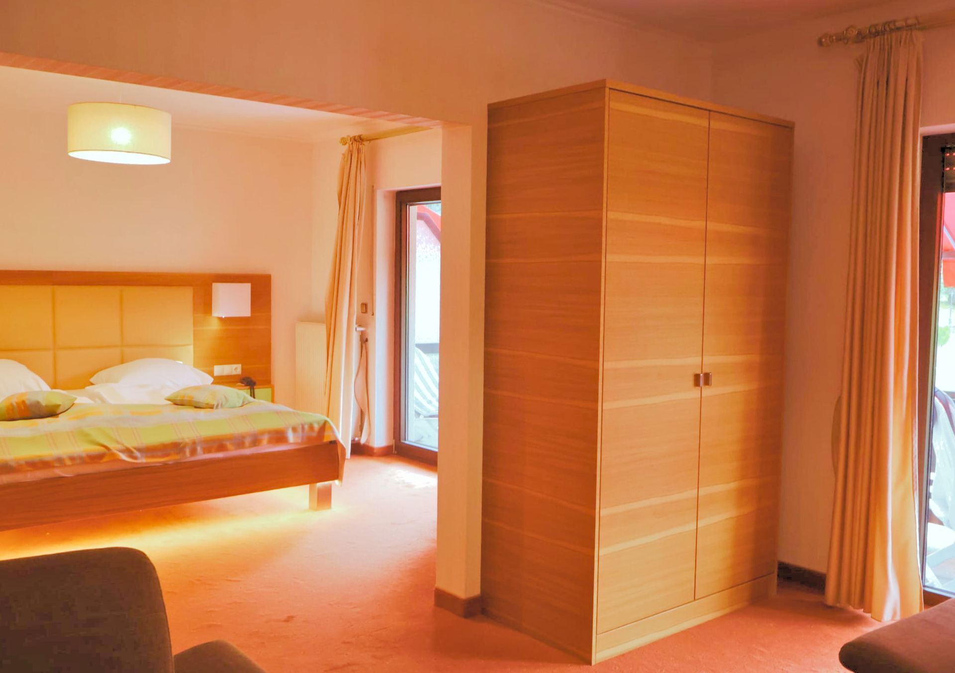 Intérieur d'une chambre d'hôtel avec lit, armoire et accès au balcon. Moquette orange vif et éclairage chaleureux.
