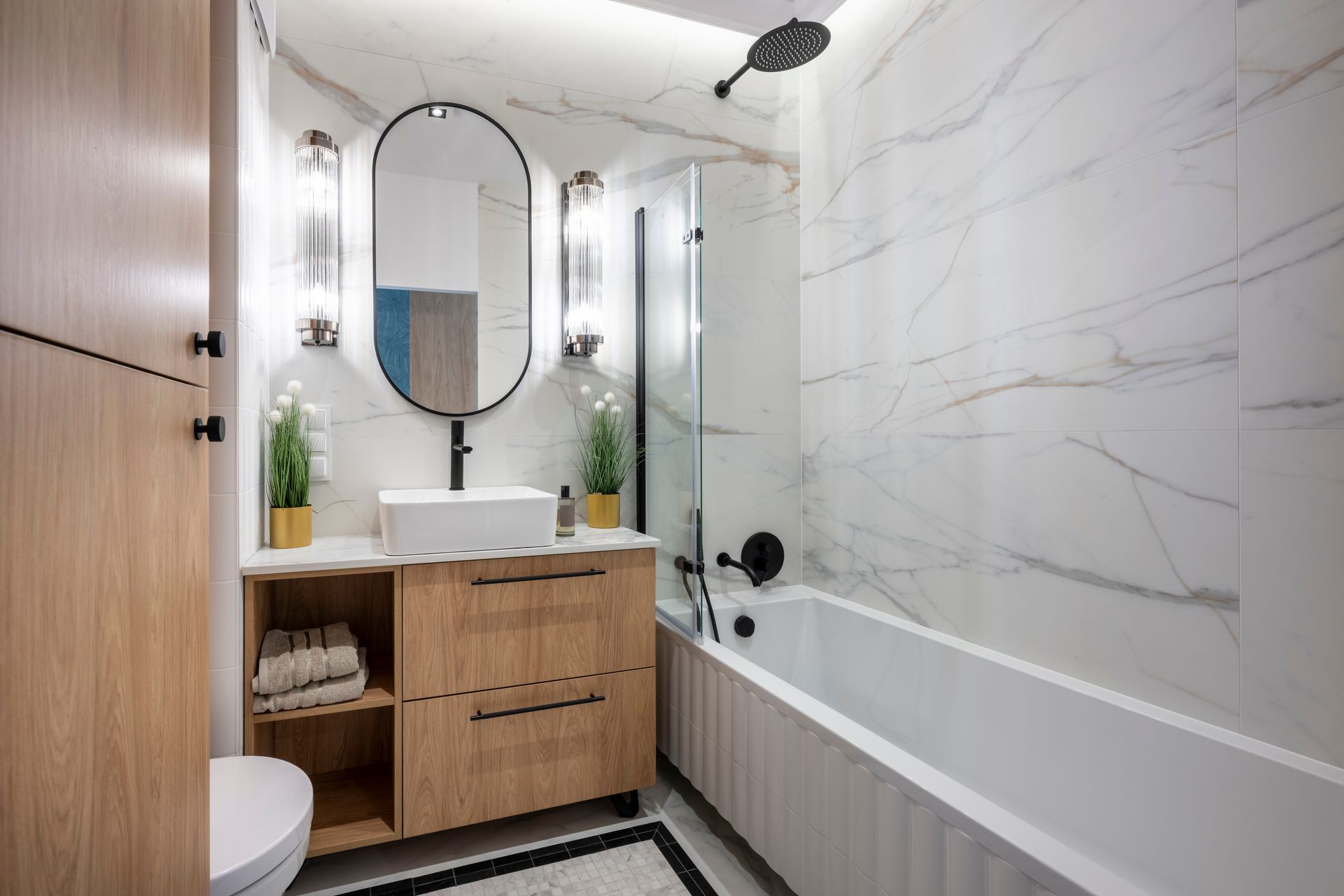 Modern bathroom with wooden vanity, white tub, marble walls, and black fixtures.