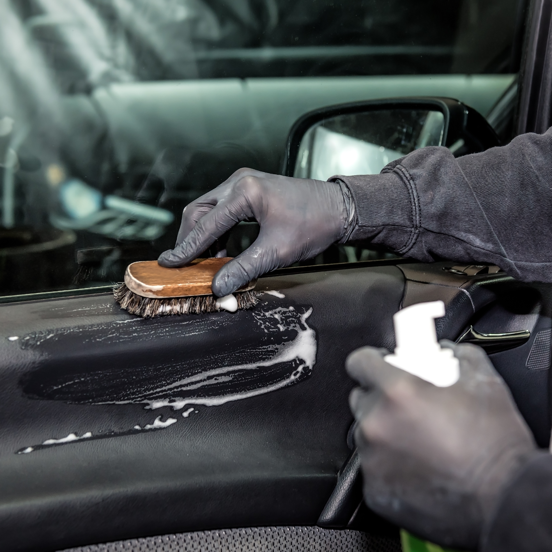Person cleaning car door panel with brush and spray bottle.