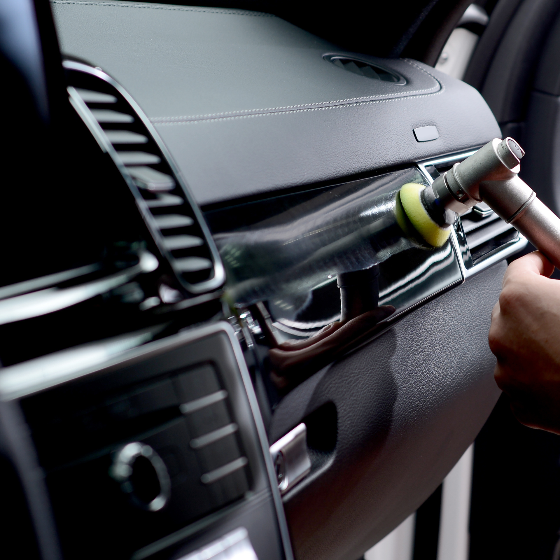 A person using a polishing tool on a shiny black car dashboard.