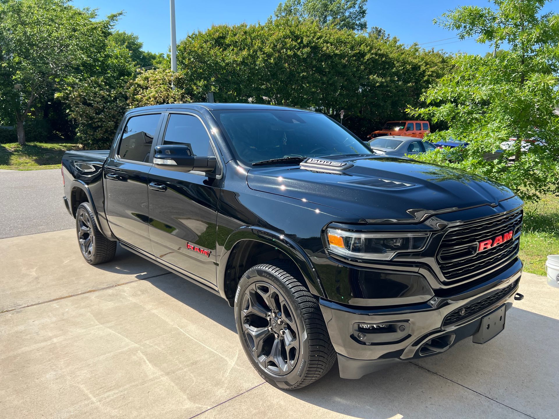 Black RAM pickup truck parked on a sunny driveway with trees in the background