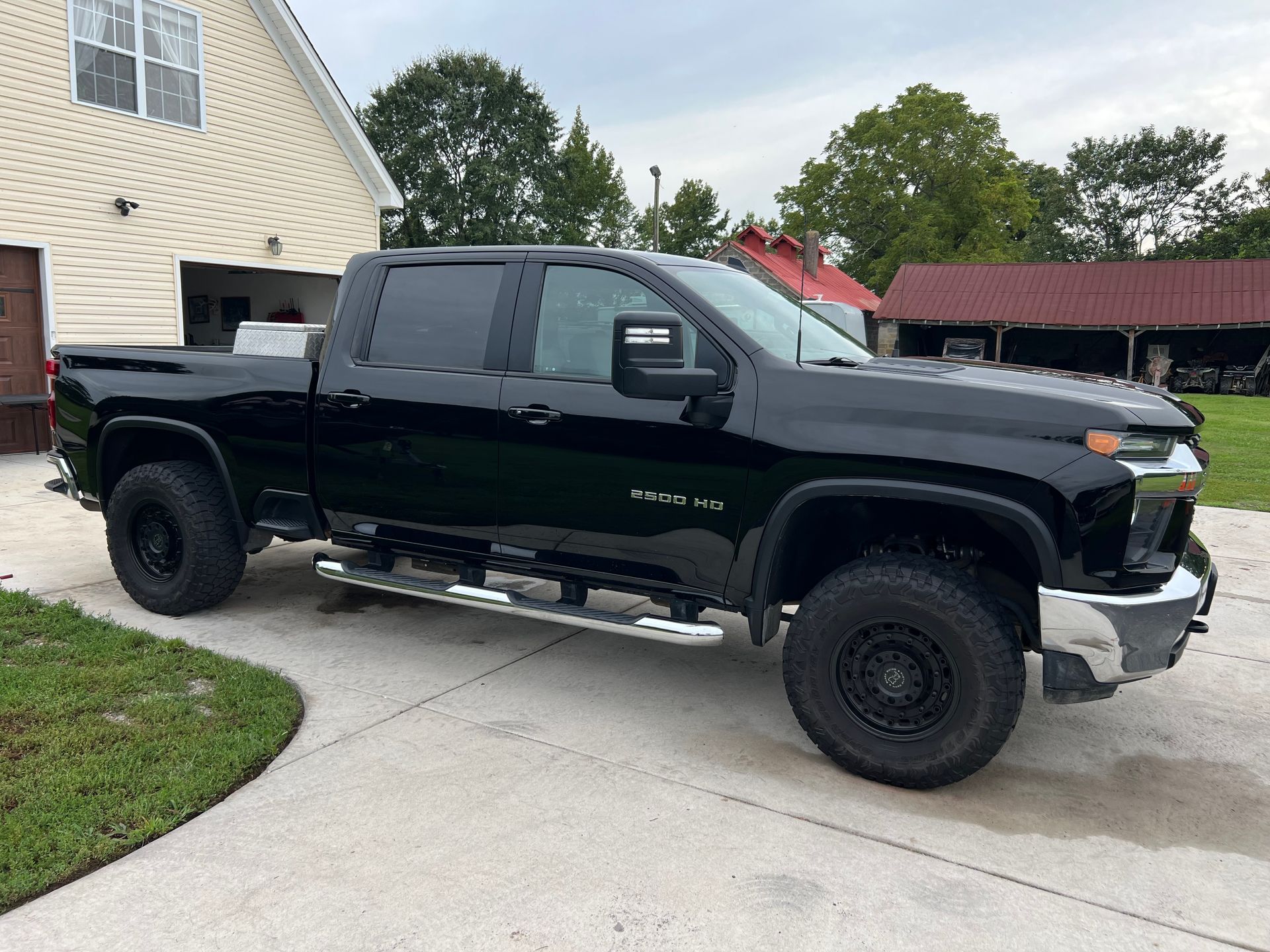 Black lifted pickup truck parked in a driveway beside a house and garage