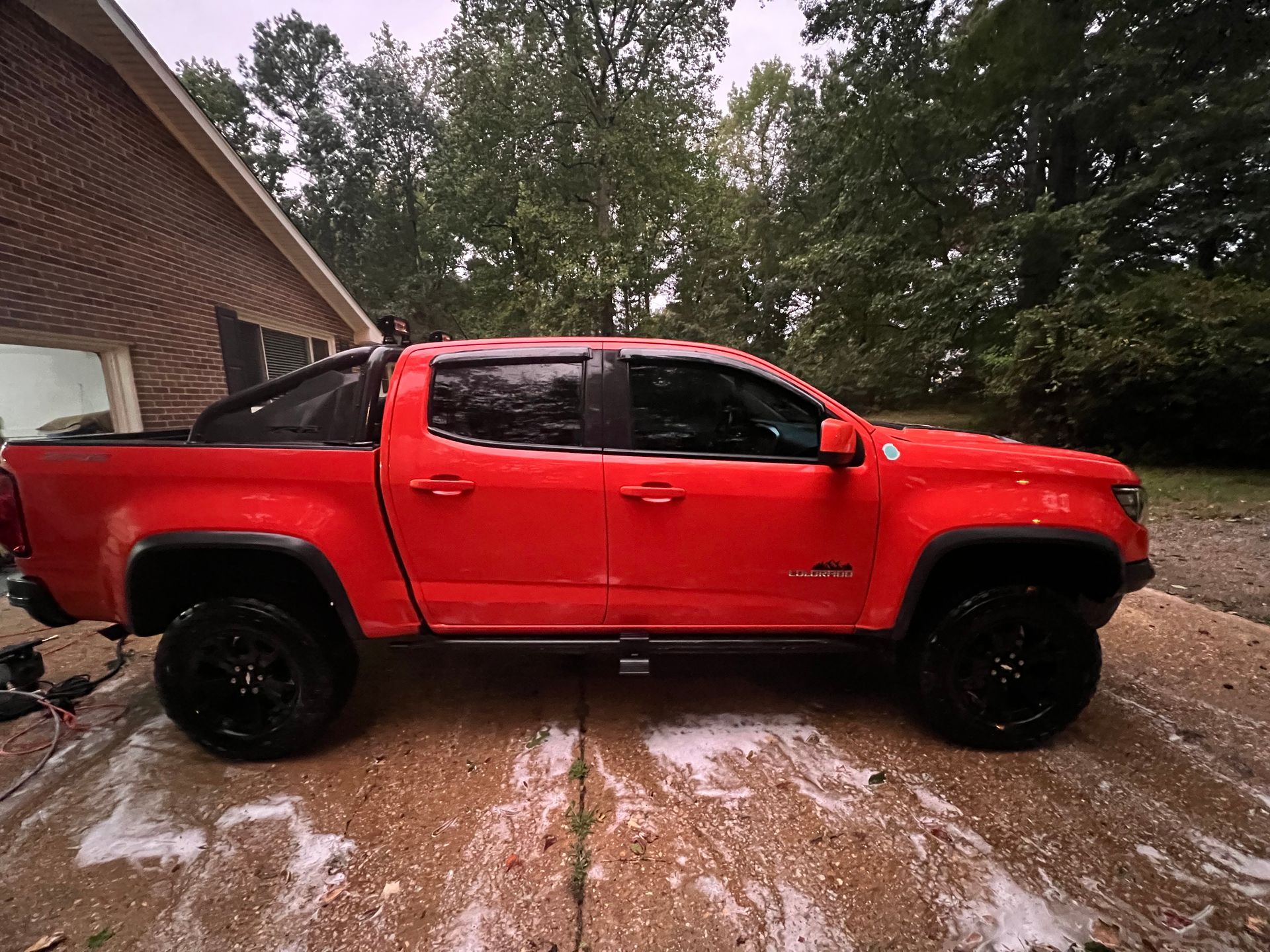 Red pickup truck parked in a driveway beside a house, with trees in the background.
