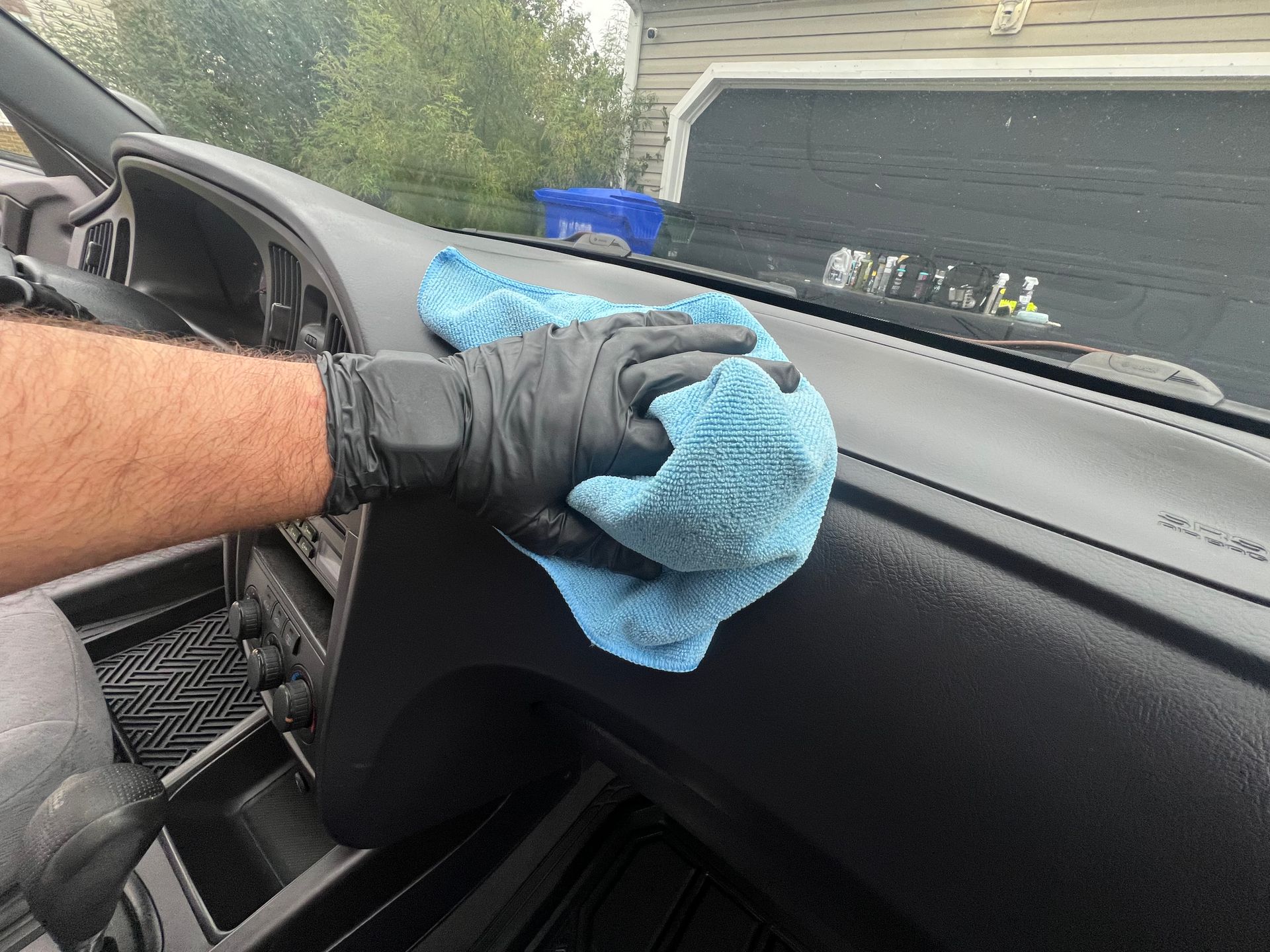 Gloved hand wiping a car dashboard with a blue microfiber cloth near the windshield.