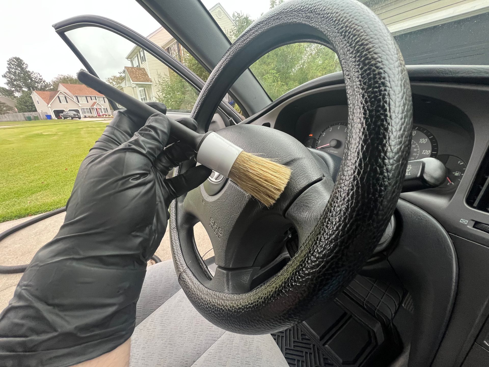 Gloved hand cleaning a car steering wheel with a brush inside the vehicle