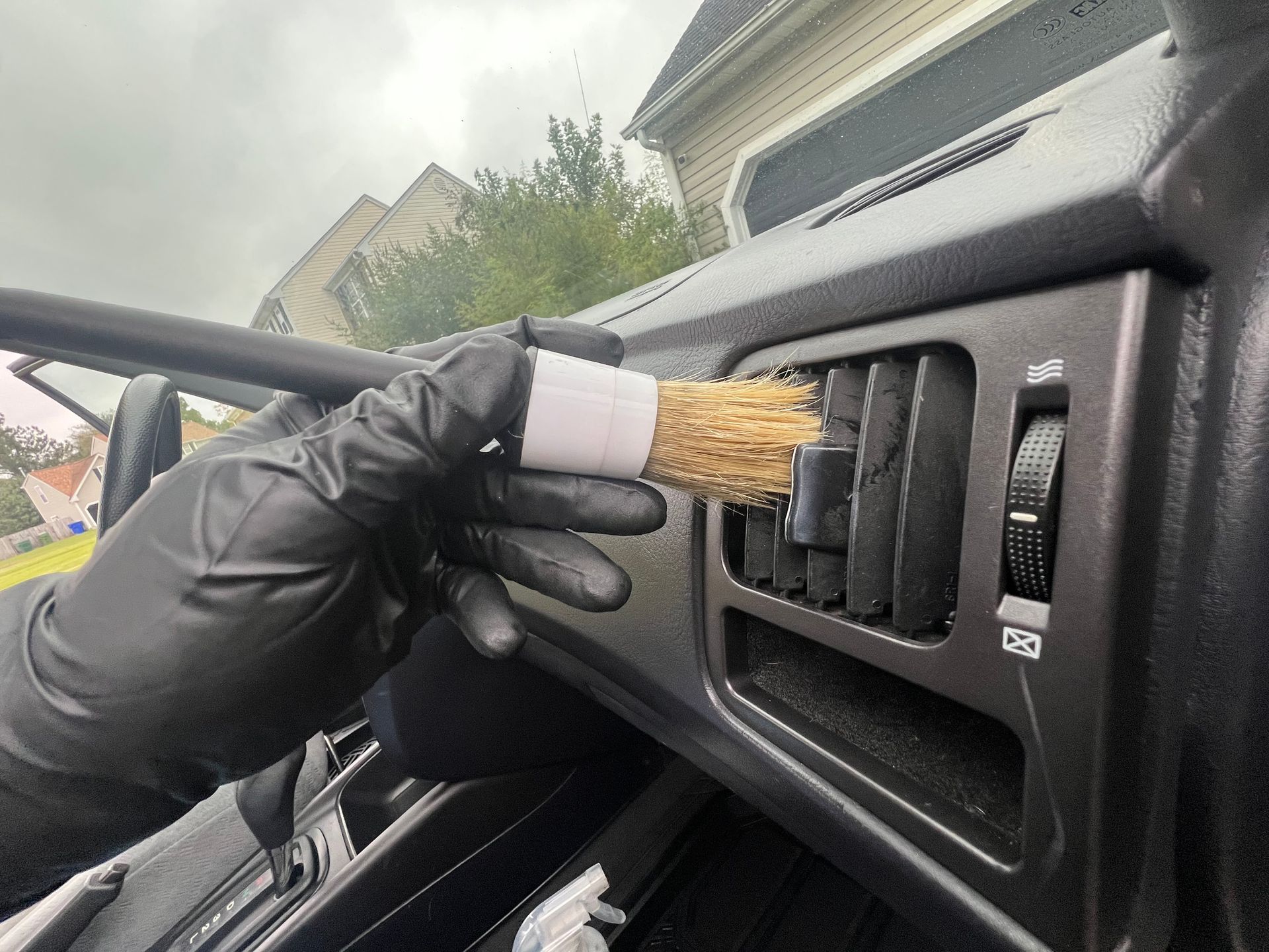 Gloved hand cleaning black car dashboard air vent with a brush
