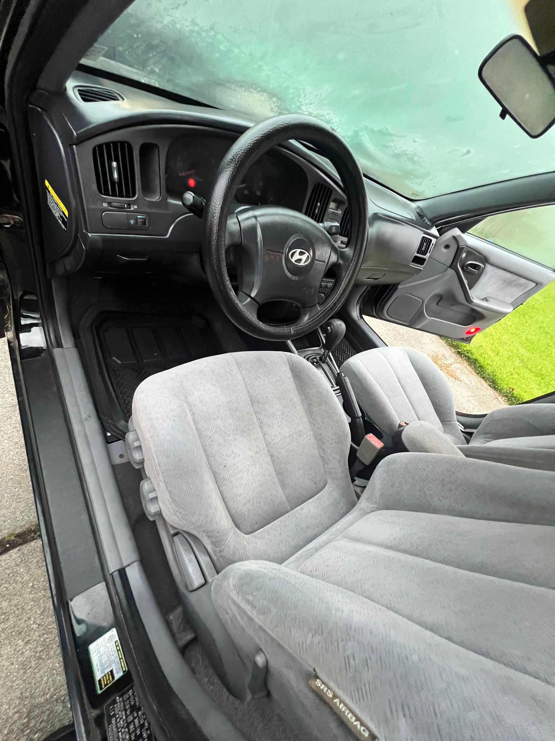 Driver’s seat and steering wheel inside a gray car interior, viewed from the open door