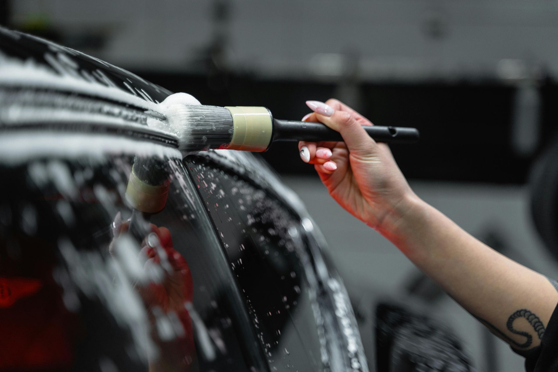Hand with brush cleaning a black car, covered in suds.