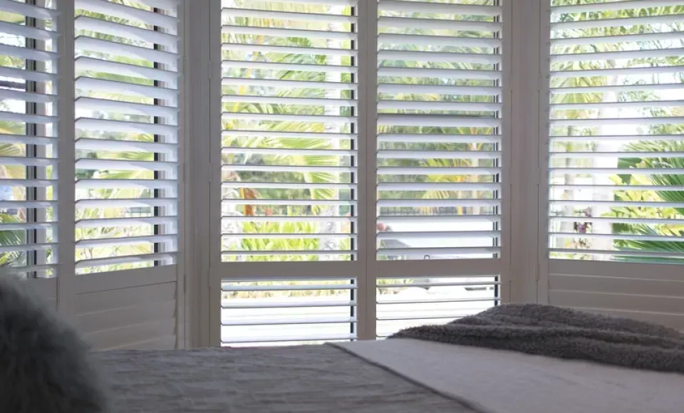 A bedroom with a bed and shutters on the windows.