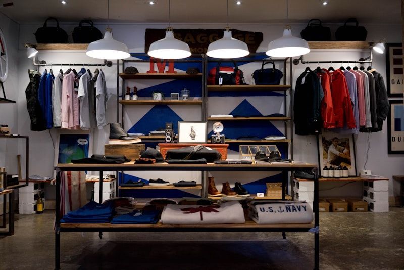 Clothing store interior with folded shirts, hanging jackets, and shelves under pendant lights
