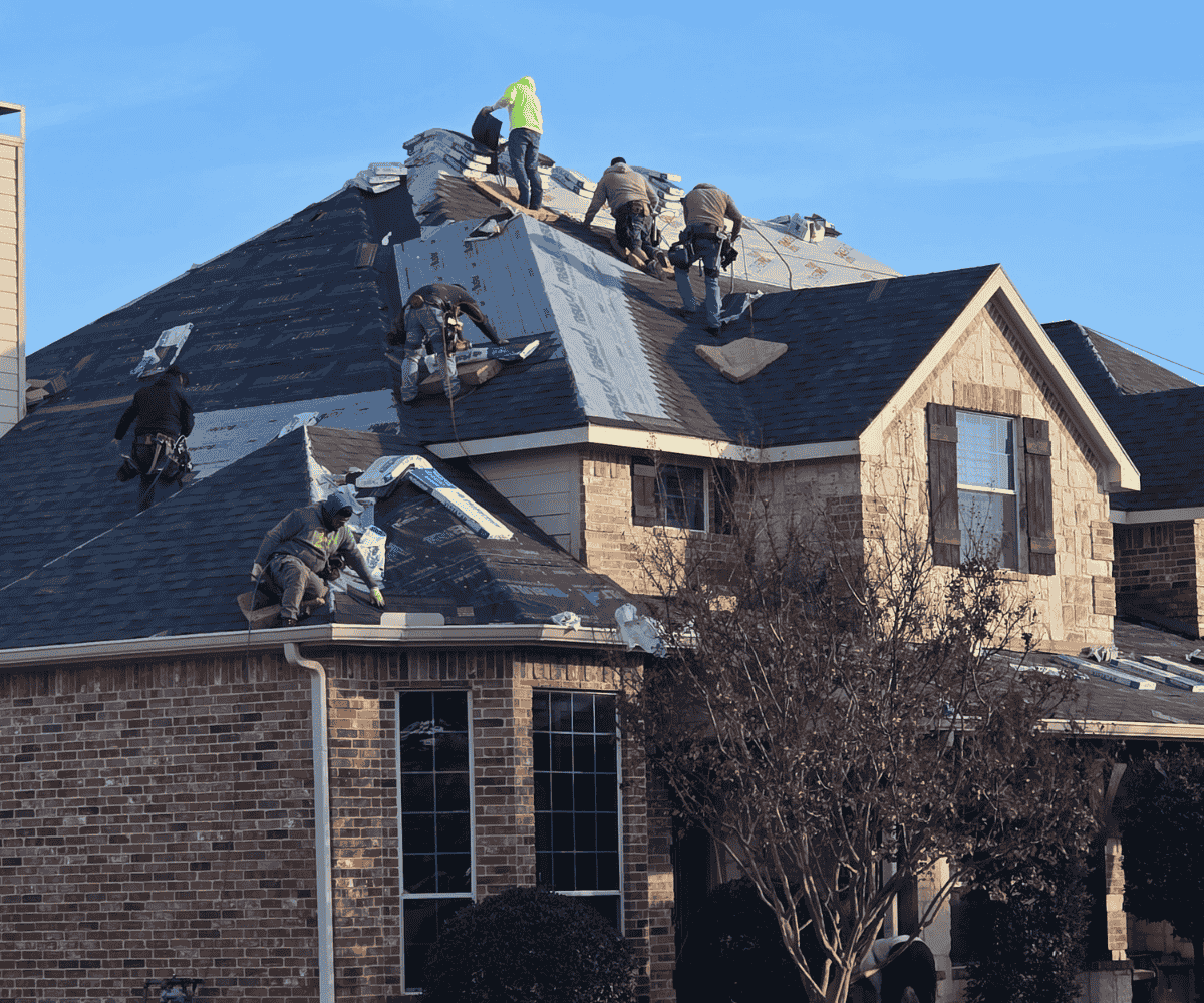 Roofers working on a house roof under repair, with shingles being replaced on a sunny day