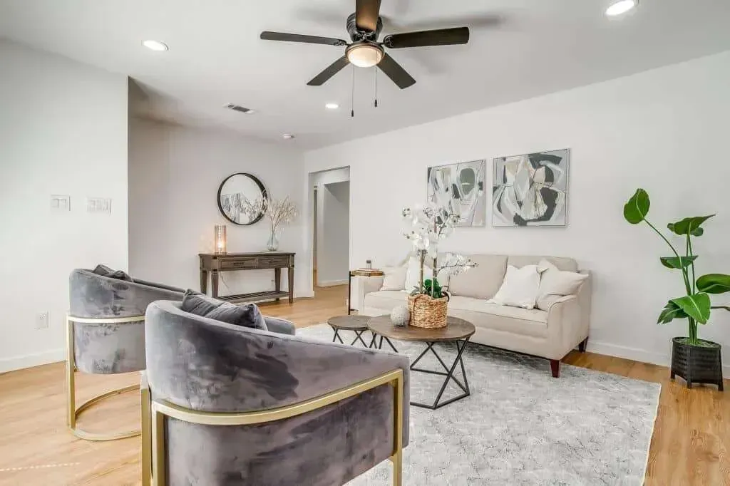 Bright modern living room with gray chairs, cream sofa, coffee table, wall art, and ceiling fan