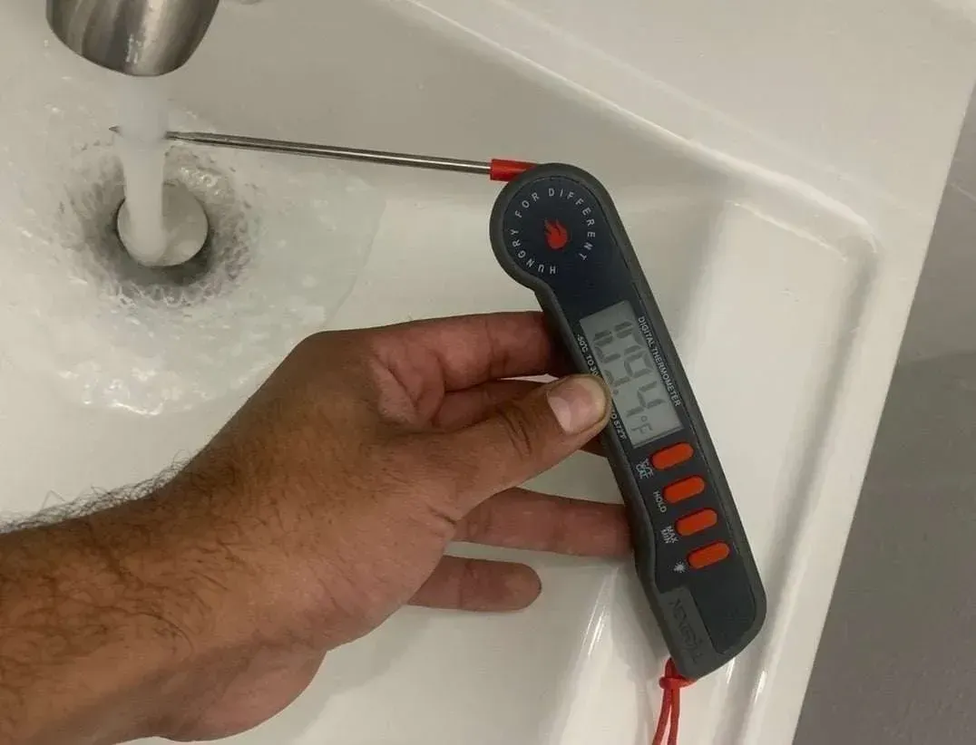 Hand holding a digital thermometer under running water in a sink