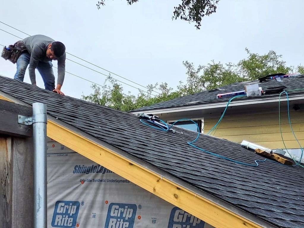 Worker on a roof installing shingles near exposed underlayment and roofing tools