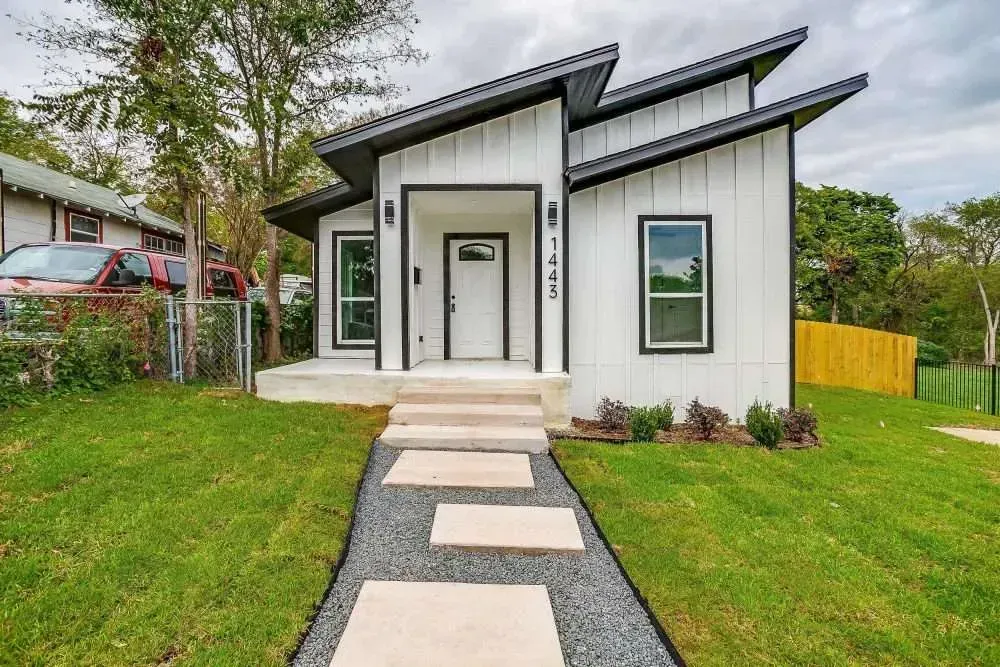 Modern white house with black roof, front steps, and stone path leading through a green yard
