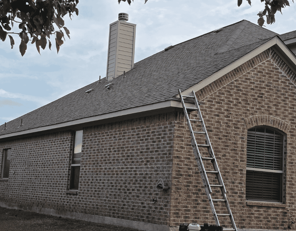 Brick house with dark shingle roof and a ladder leaning against the side under cloudy skies