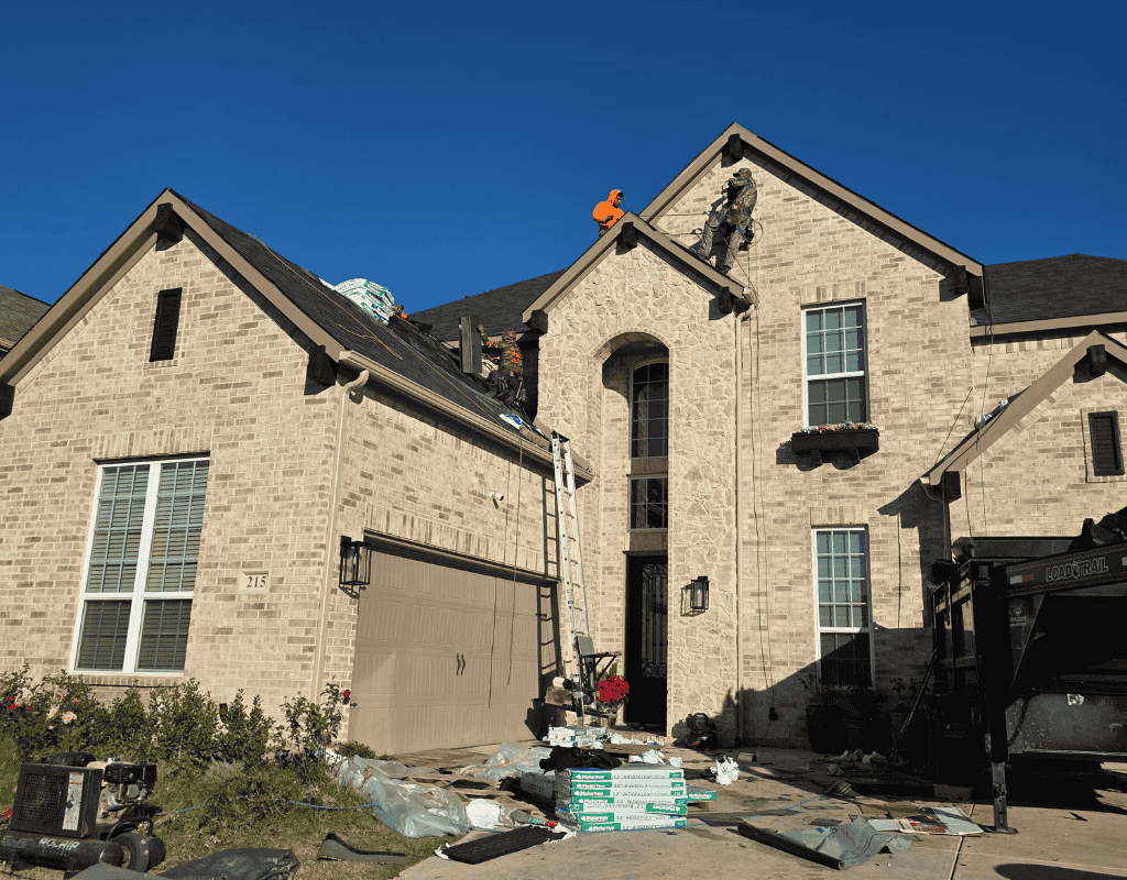 Two-story brick house under construction with debris in front and a worker on the roof