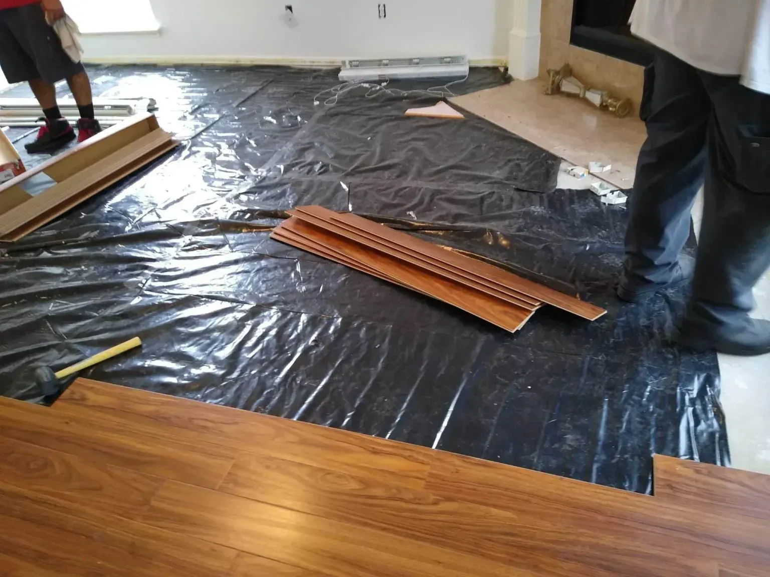 Floor renovation in progress with black underlayment, wooden planks, and a person standing nearby.
