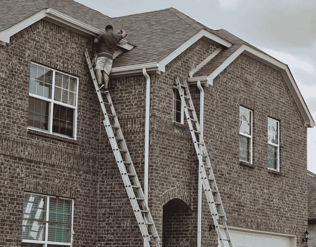 Worker on a ladder repairing a brick house roof near a dormer window