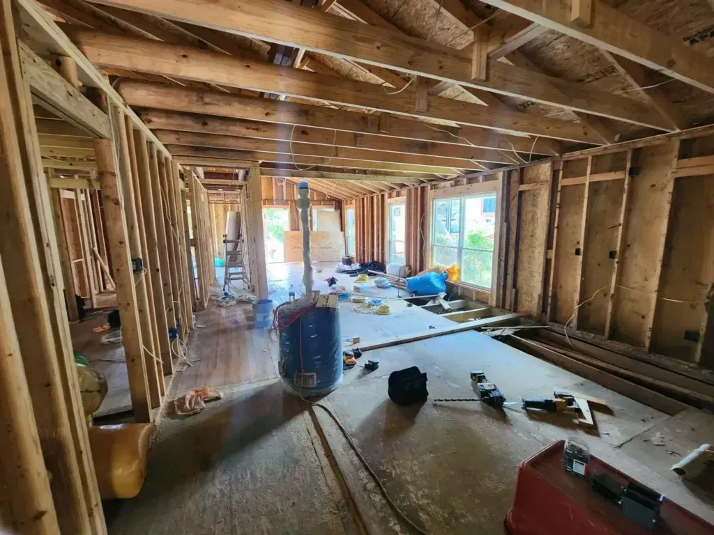 Framed house interior under construction with exposed beams, scattered tools, and drywall materials.