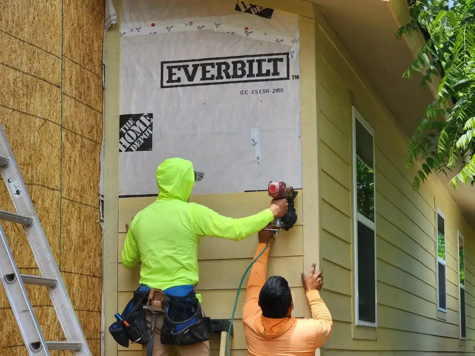Workers installing house siding and trim with power tools on an exterior wall.