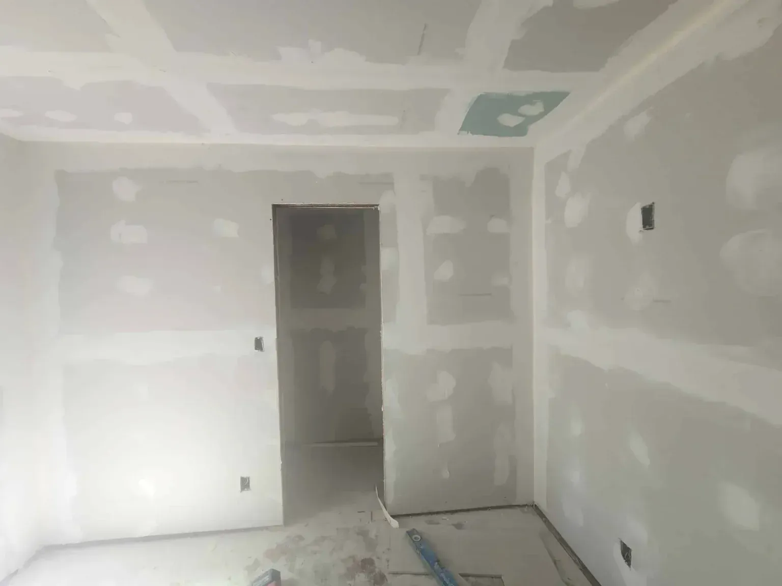 Unfinished drywall room with open doorway and visible patching on walls and ceiling.