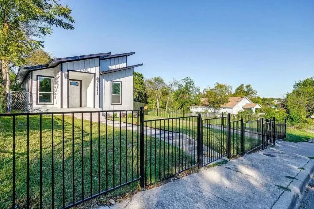 Modern house behind black fence with gravel driveway and green yard under blue sky