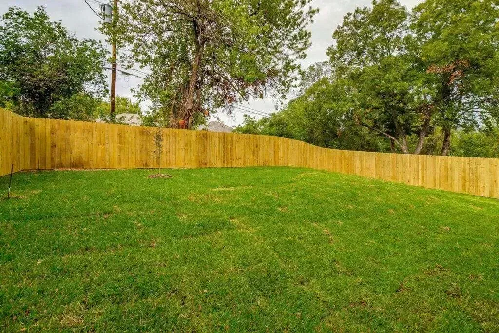 Grassy yard bordered by a yellow wooden fence with trees in the background.