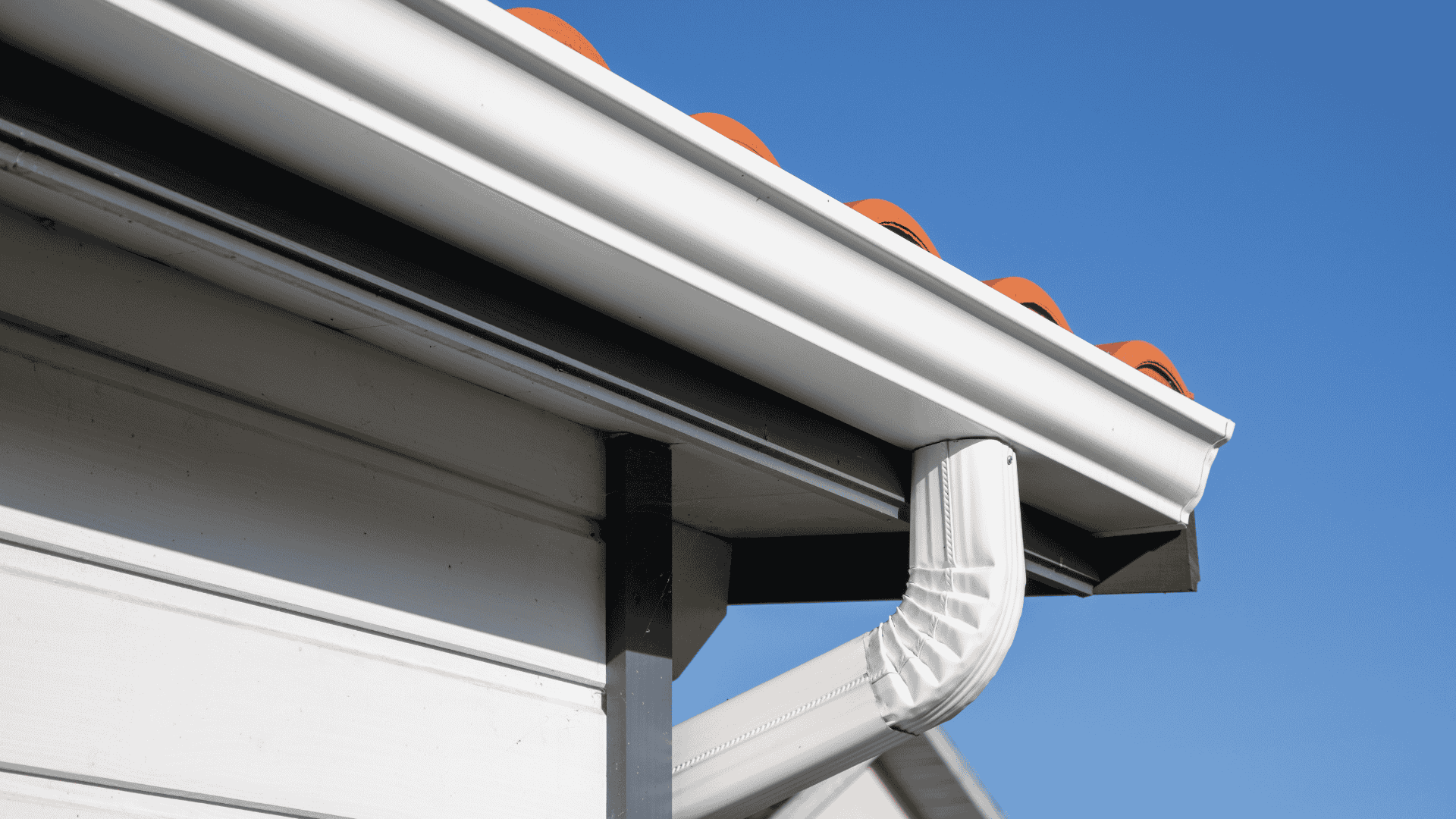 White gutter and downspout on a house roof against a clear blue sky