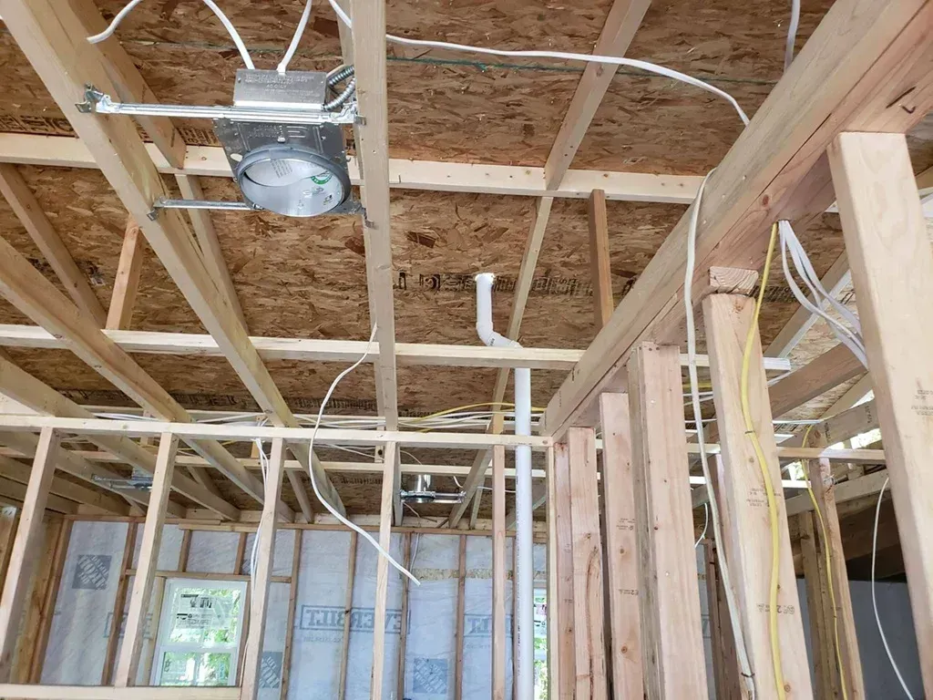 Unfinished room framing with exposed wooden studs, ceiling joists, wiring, and a hanging light fixture