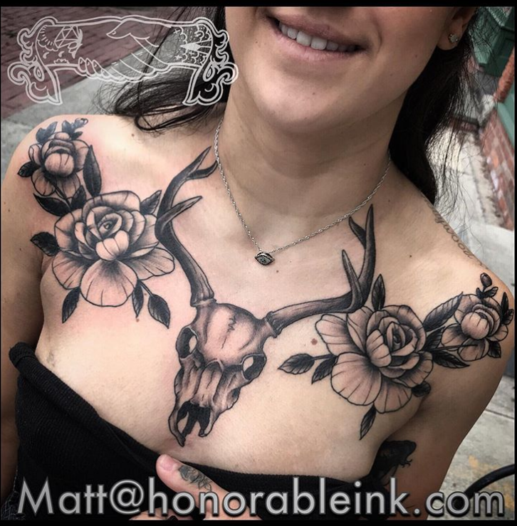 Woman wearing large black floral and deer skull chest tattoos, smiling with shoulders bare