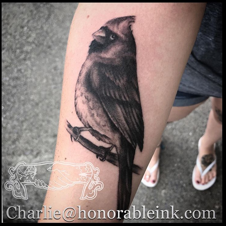 Black bird tattoo on a person's calf, perched on a branch.