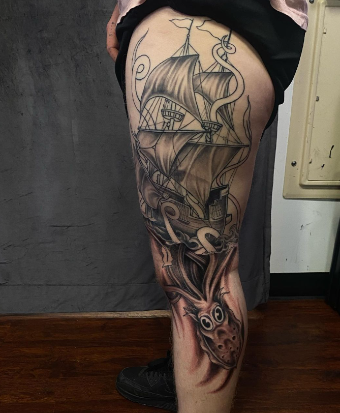 Person showing a large black-and-gray tattoo sleeve on their leg, featuring birds and floral designs.