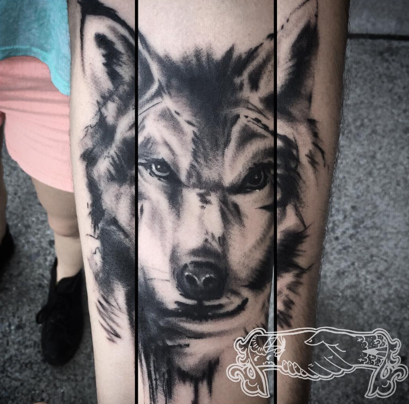 Black-and-gray wolf tattoo on a person’s forearm, shown in close-up.